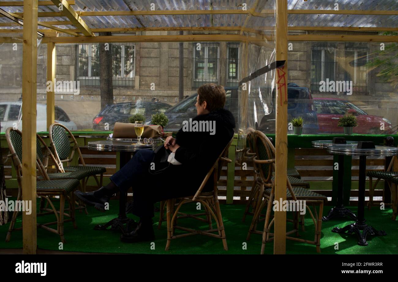 A Parisian woman sits alone, enjoying a drink and cigarette on the temporary terrace of a cafe in Paris after Covid-19 restrictions were lifted in 2021 - Le Montmartre Café, Rue Custine, 75018, Paris, France Stock Photo