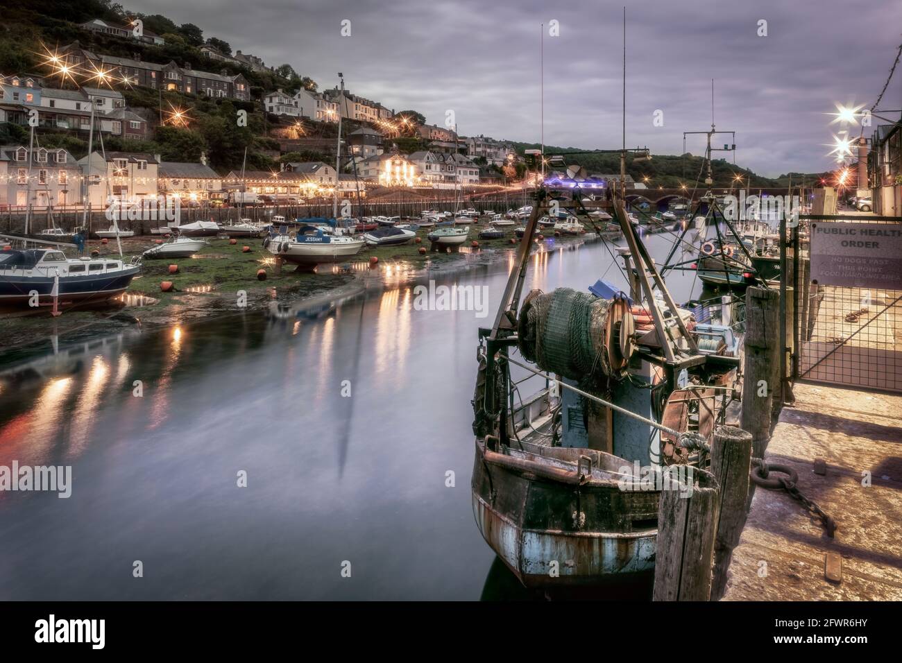 After another chilly overcast day the lights flicker on as the daylight gives way to dusk in the historic fishing port of Looe in Cornwall. Stock Photo