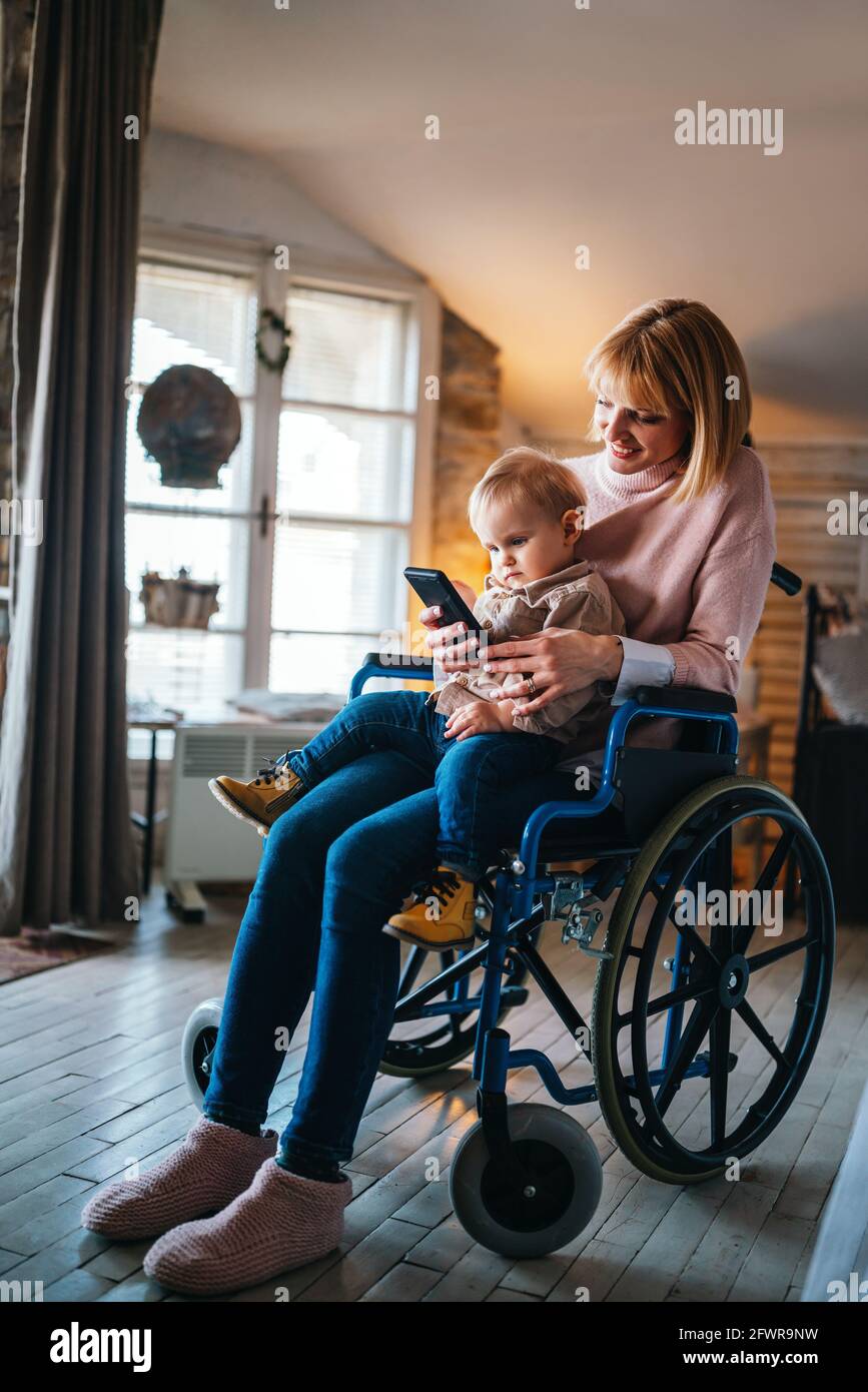 Happy smiling mother with disability in wheelchair playing with child at home Stock Photo