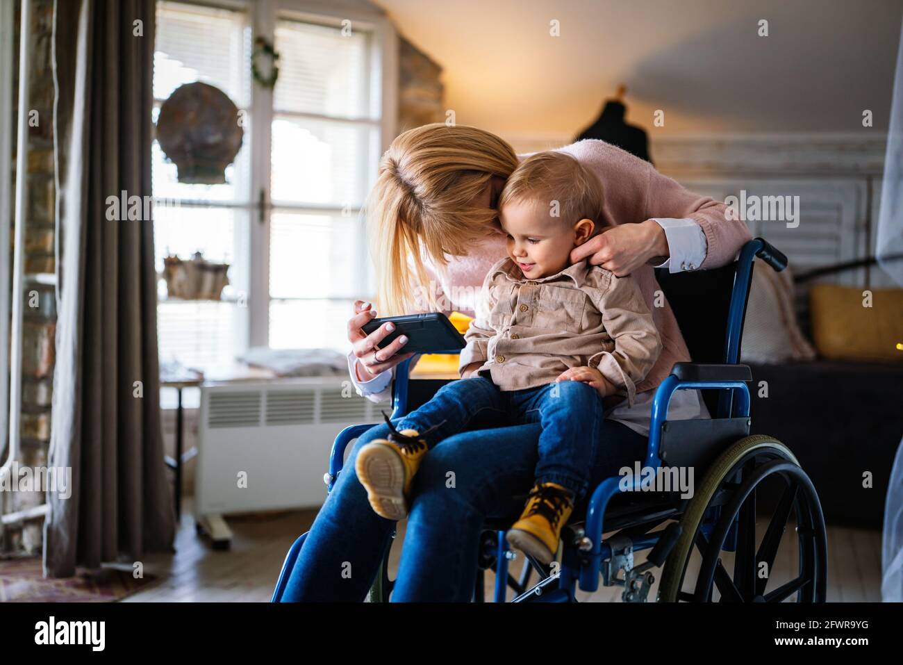 Happy smiling mother with disability in wheelchair playing with child at home Stock Photo