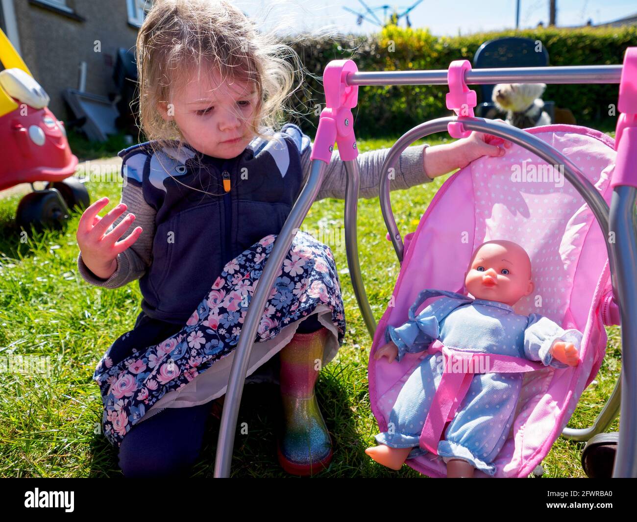 Toddler playing in the garden with a baby doll in a swing chair, UK Stock Photo