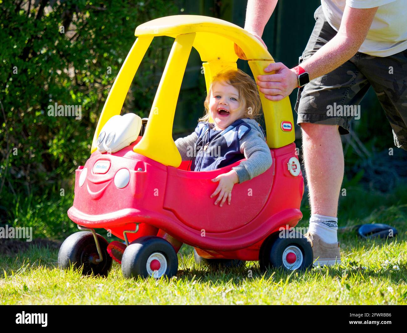 Dad pushing toddler in Little Tikes toy car, UK Stock Photo