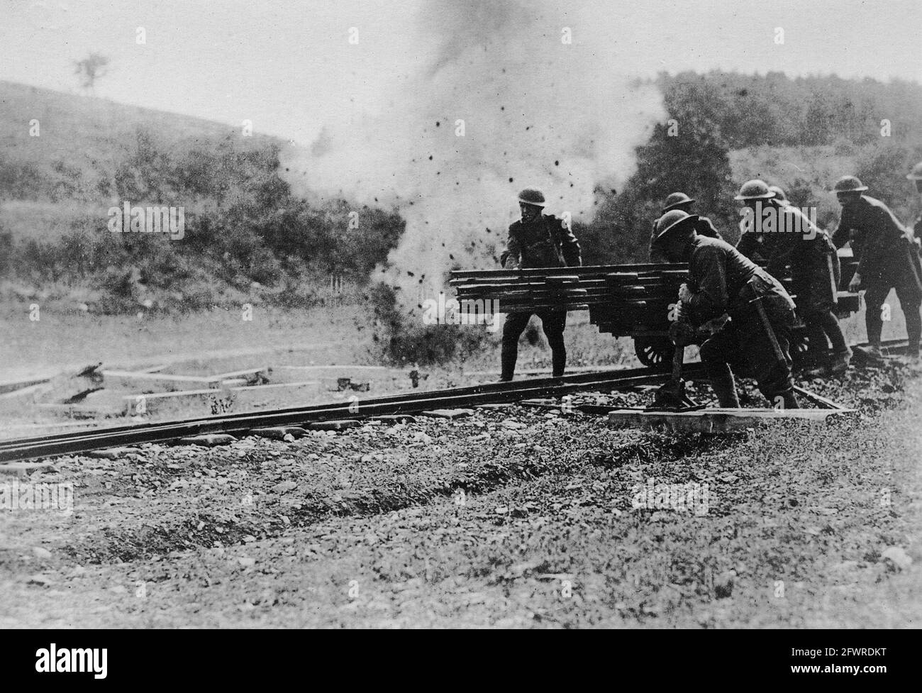 U.S. army engineers working under fire. The bursting of a high explosive shell nearby does not phase these American engineers who are repairing a narrow gauge track recently damaged by enemy artillery. Stock Photo