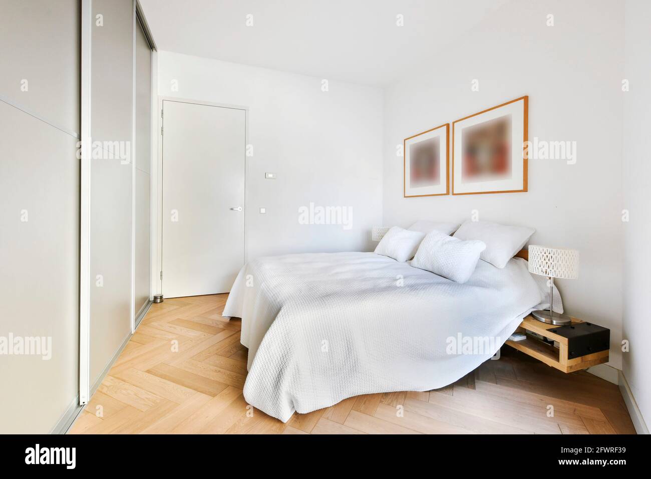 Comfortable bed with white linen and cushions in light room with frames