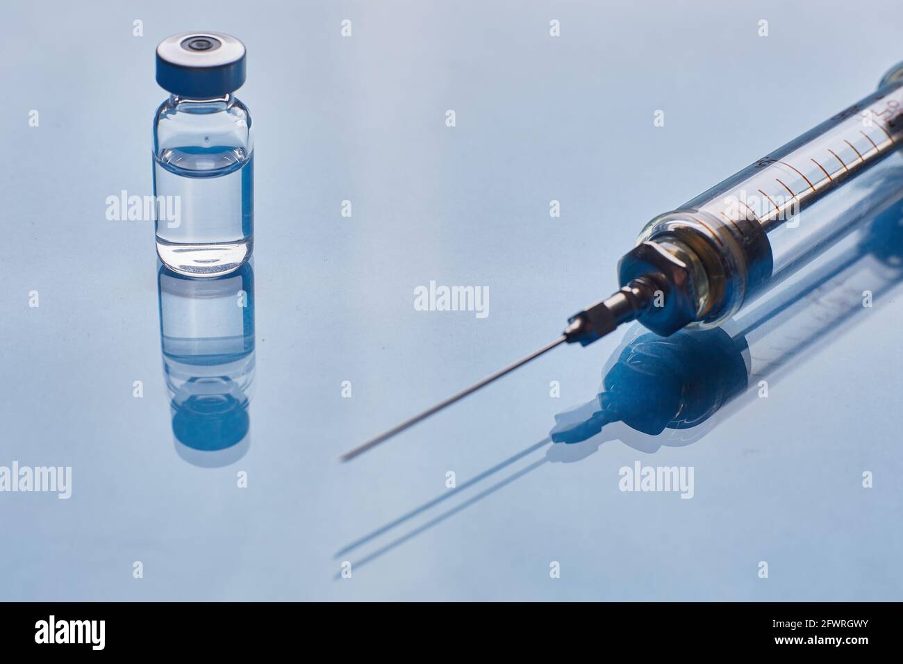 Glass vaccine vial and glass medical syringe on blue glass background ...