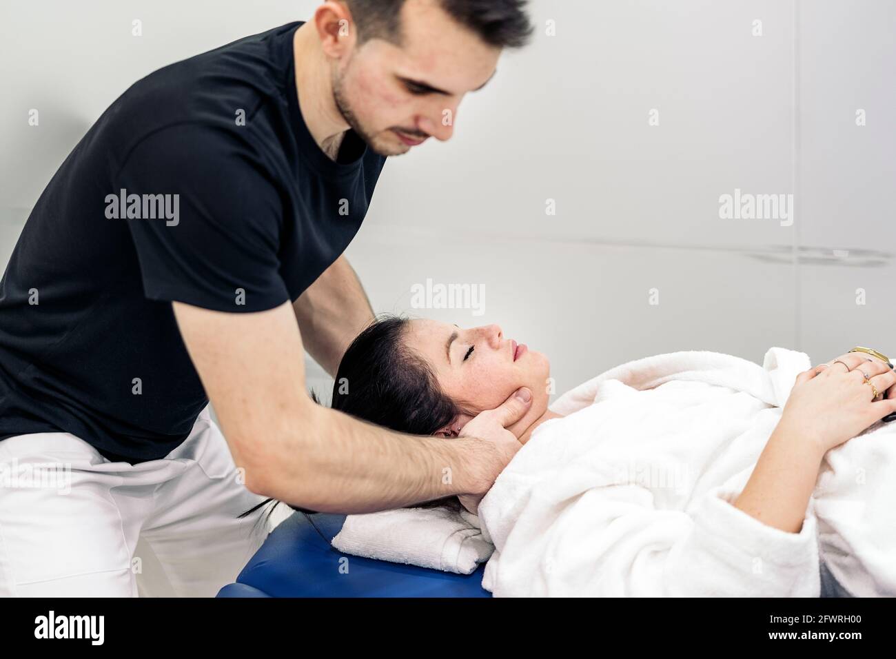 Male physiotherapist giving neck massage to relaxed woman lying in stretcher. Stock Photo
