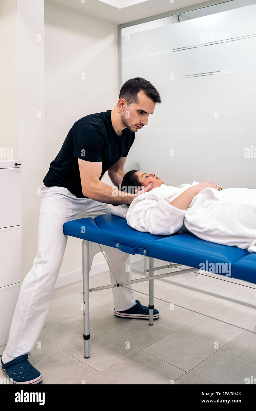 Male physiotherapist giving neck massage to relaxed woman lying in stretcher. Stock Photo