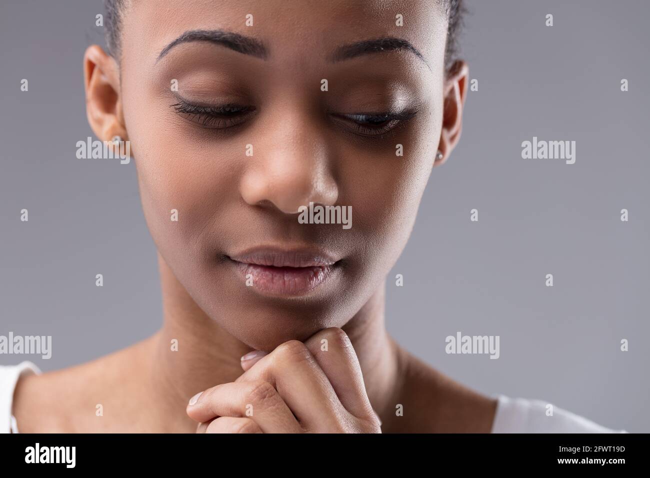 Cropped portrait of the face of a serious young Black woman with downcast eyes glancing to the side with her hand to her chin Stock Photo