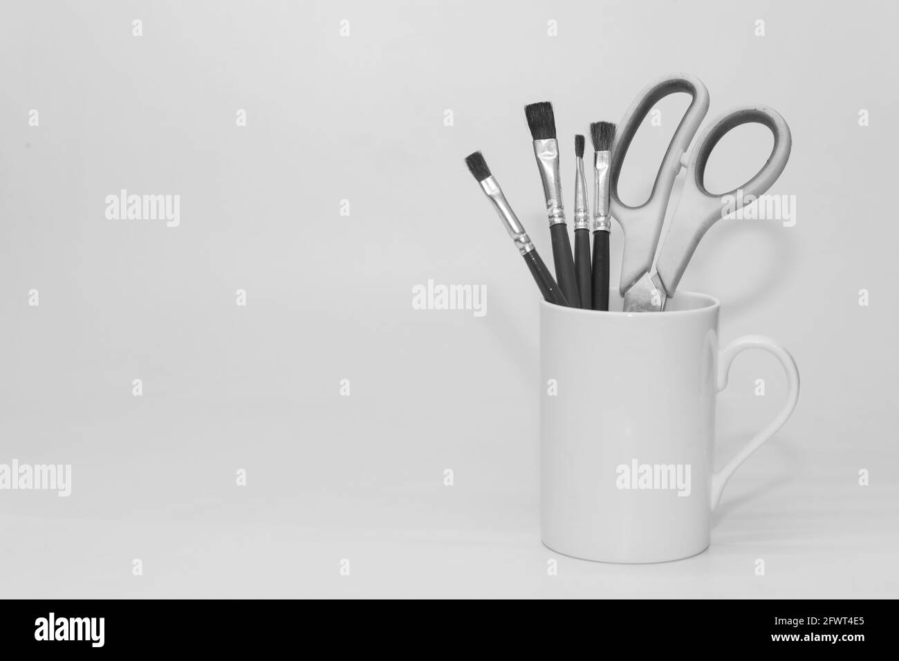 Paint brushes and a scissors kept inside a white ceramic mug in