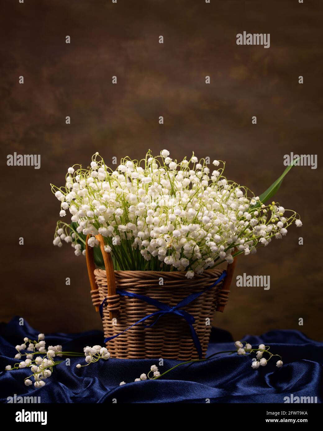 Still life with a bouquet of lilies of the valley in a wicker basket ...