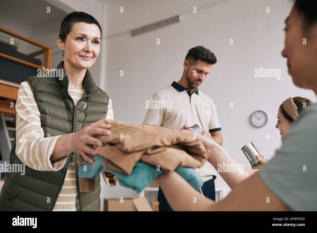 Portrait of mature woman giving used clothes to volunteers during help and donations event, copy space Stock Photo