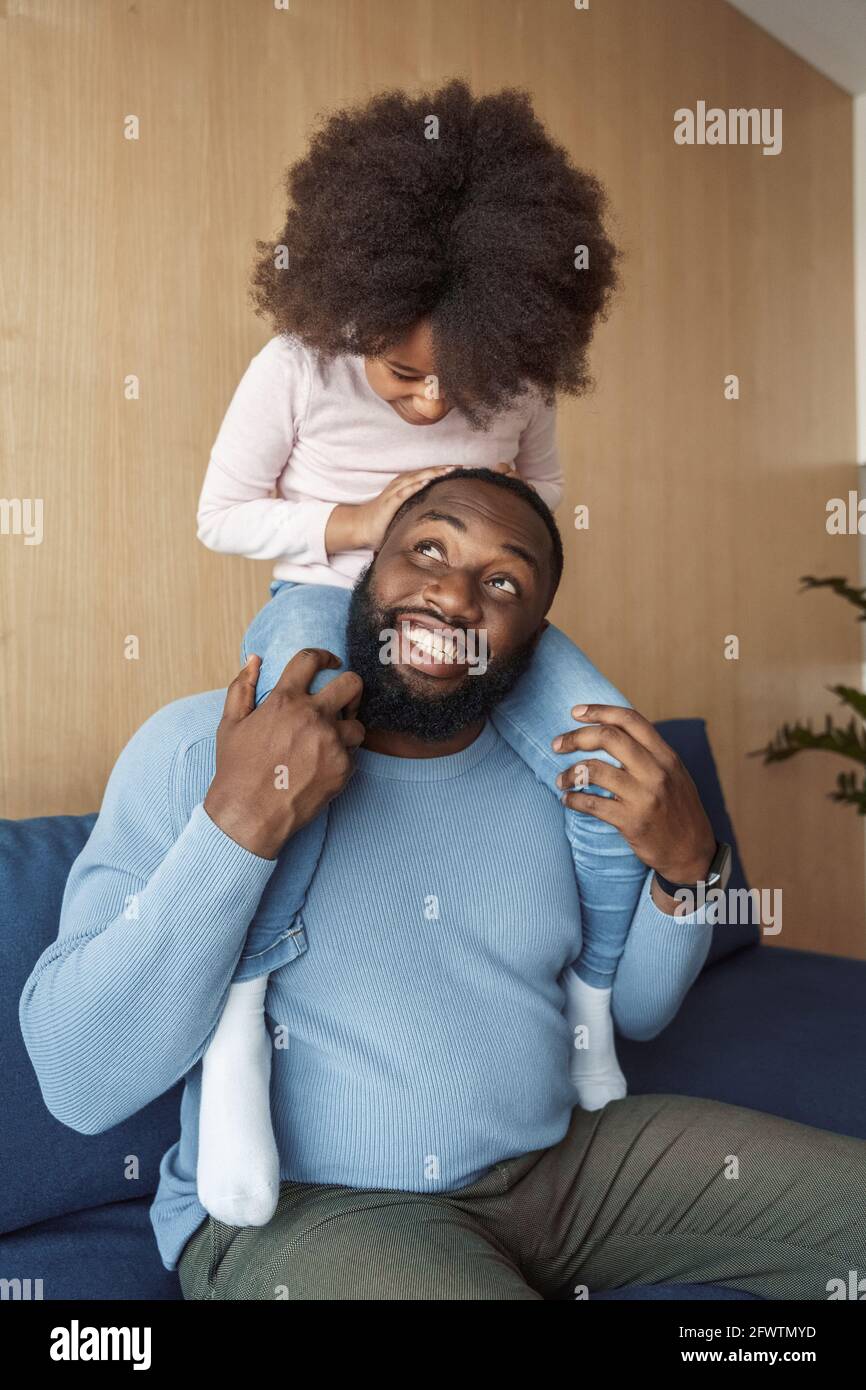 Happy african american father holding daughter on shoulder indoor ...