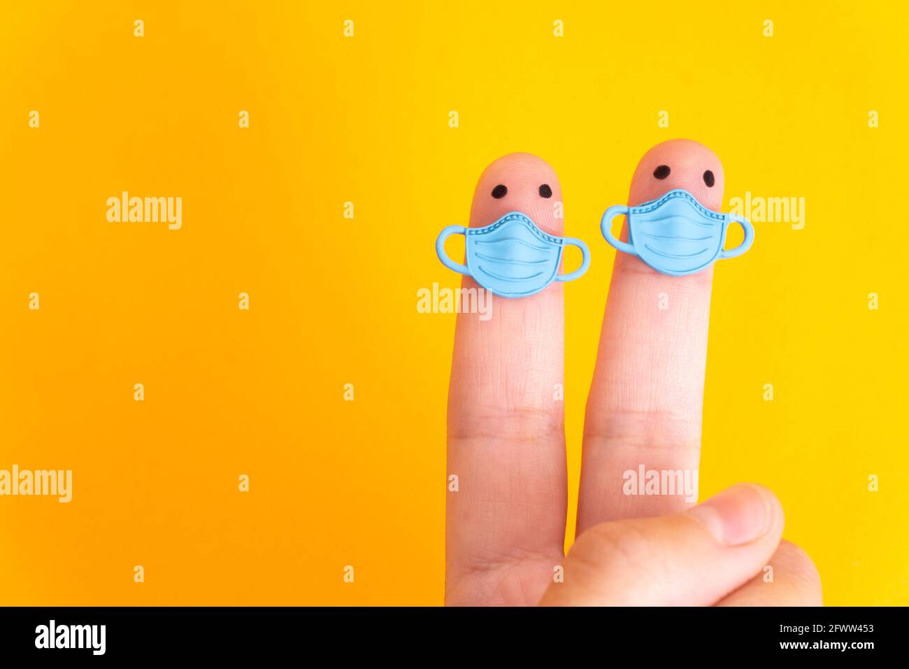 Two finger characters wearing blue face masks isolated on yellow background Stock Photo
