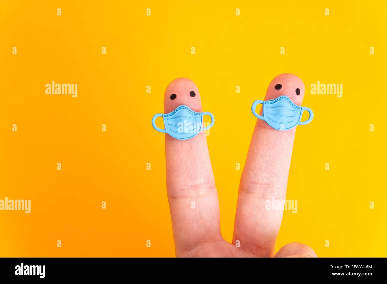 Two finger characters wearing blue face masks while keeping distance isolated on yellow. The concept of physical distancing to prevent the spread of t Stock Photo