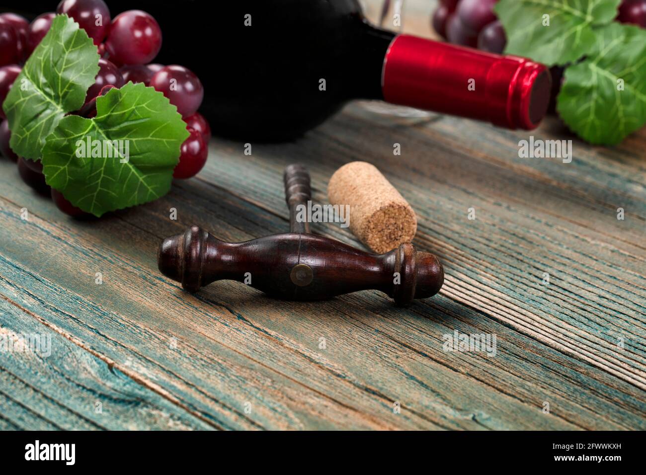 Select focus of vintage corkscrew with grapes and wine bottle in background on blue rustic wood planks Stock Photo