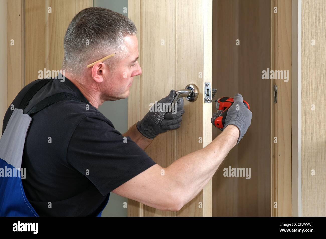 Handyman carpenter installs an internal door lock. Wooden interior door