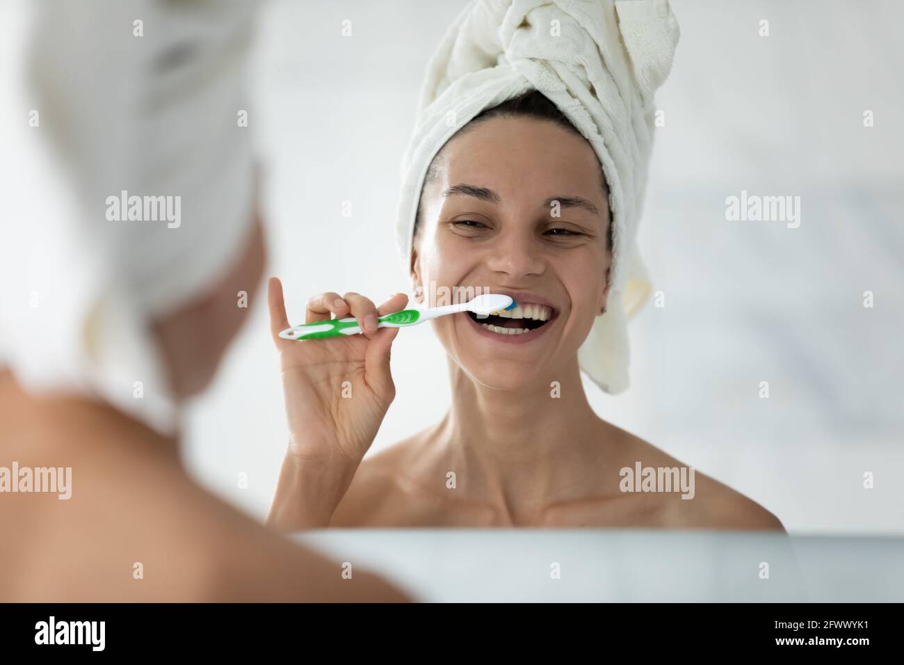 Joyful girl smiling while brushing perfect white teeth after shower
