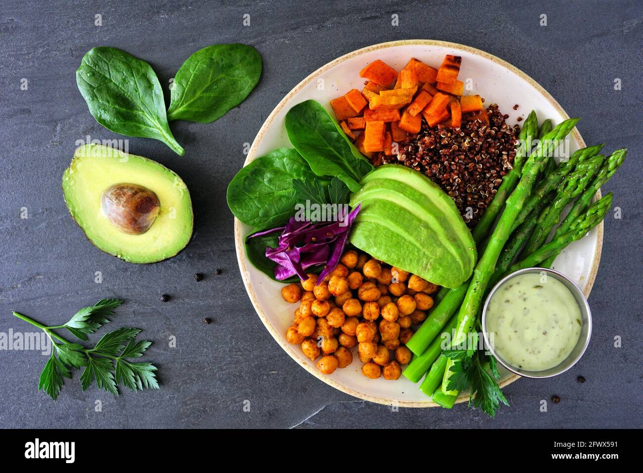 Healthy Buddha bowl with asparagus, quinoa, sweet potato, chickpeas and avocado. Top view over a dark slate background. Stock Photo
