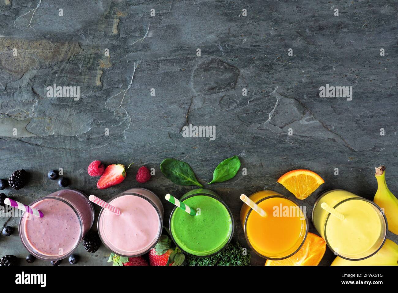 Assorted healthy fruit smoothies in. Top view bottom border against a dark background. Copy space. Stock Photo