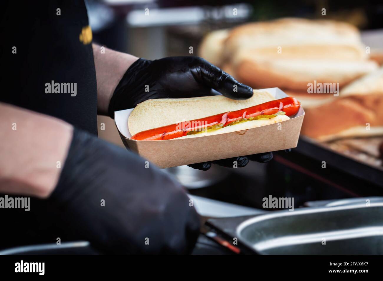 Hands of chef making fresh hot dog with vegetables and sauce. Grilled sausage in bun. Fast food, Barbecue, grill concept Stock Photo