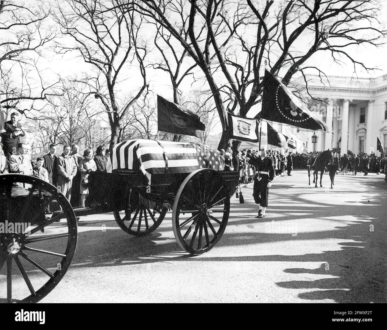 The funeral procession of President John F. Kennedy departs the White House for the Cathedral of St. Matthew the Apostle; the flag-draped casket of President Kennedy is borne by a horse-drawn caisson. Riderless horse, Black Jack (led by Private First Class Arthur A. Carlson), walks at right; mourners and members of the color guard line the North Lawn driveway. White House, Washington, D.C. Stock Photo