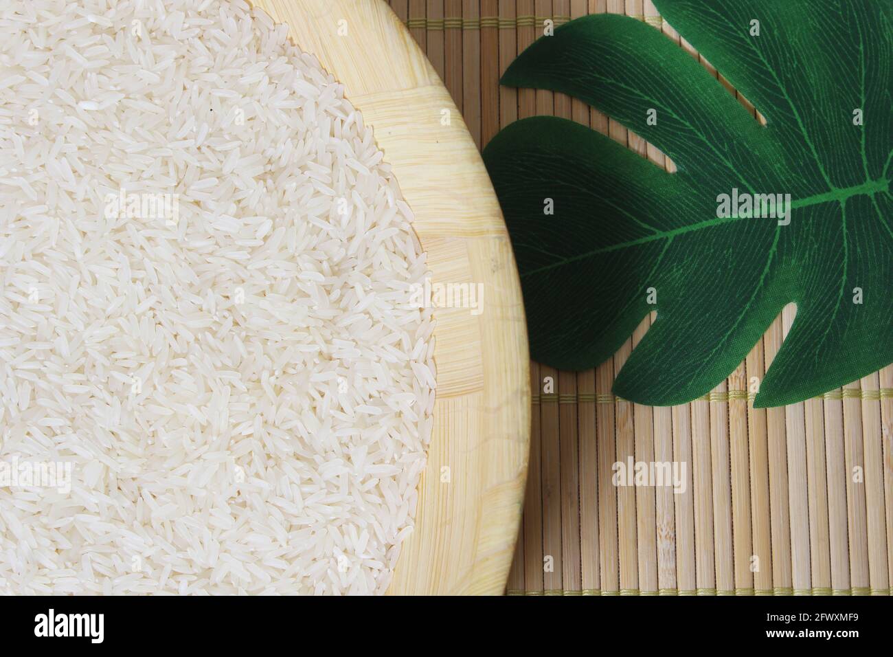 Bowl of Uncooked White Rice with leaf on bamboo mat Stock Photo