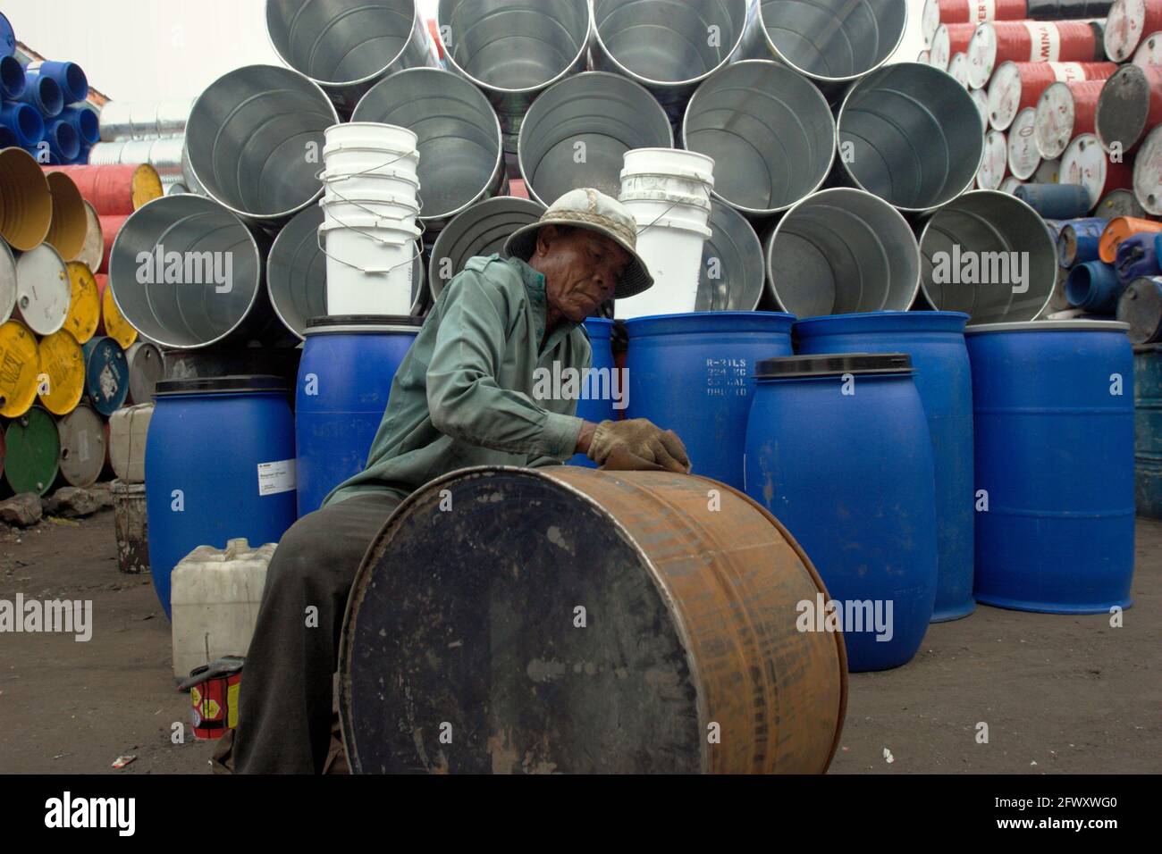 A worker cleaning a container drum at a used items trading shop in Surabaya, East Java, an Indonesian province that is seen as 'global hotspot' facing 'very significant climate change adaptation challenges' in a 2021 scientific assessment focusing on climate risk, which was published by The World Bank Group and Asian Development Bank. The rising temperature will disproportionately affect the poorest groups in society. Manual labor workers working at open spaces--commonly among the lowest paid--are among the communities being most at risk of having productivity losses due to heat stress. Stock Photo
