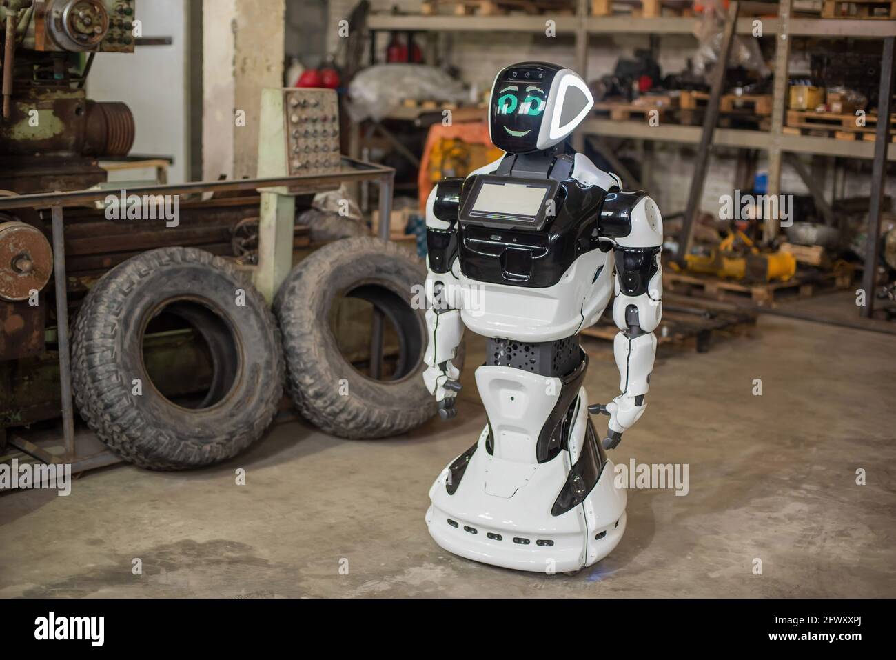 A humanoid, white robot on wheels, with a display on his chest, moves his  hands. It stands in a dirty, cluttered garage with old machines Stock Photo  - Alamy