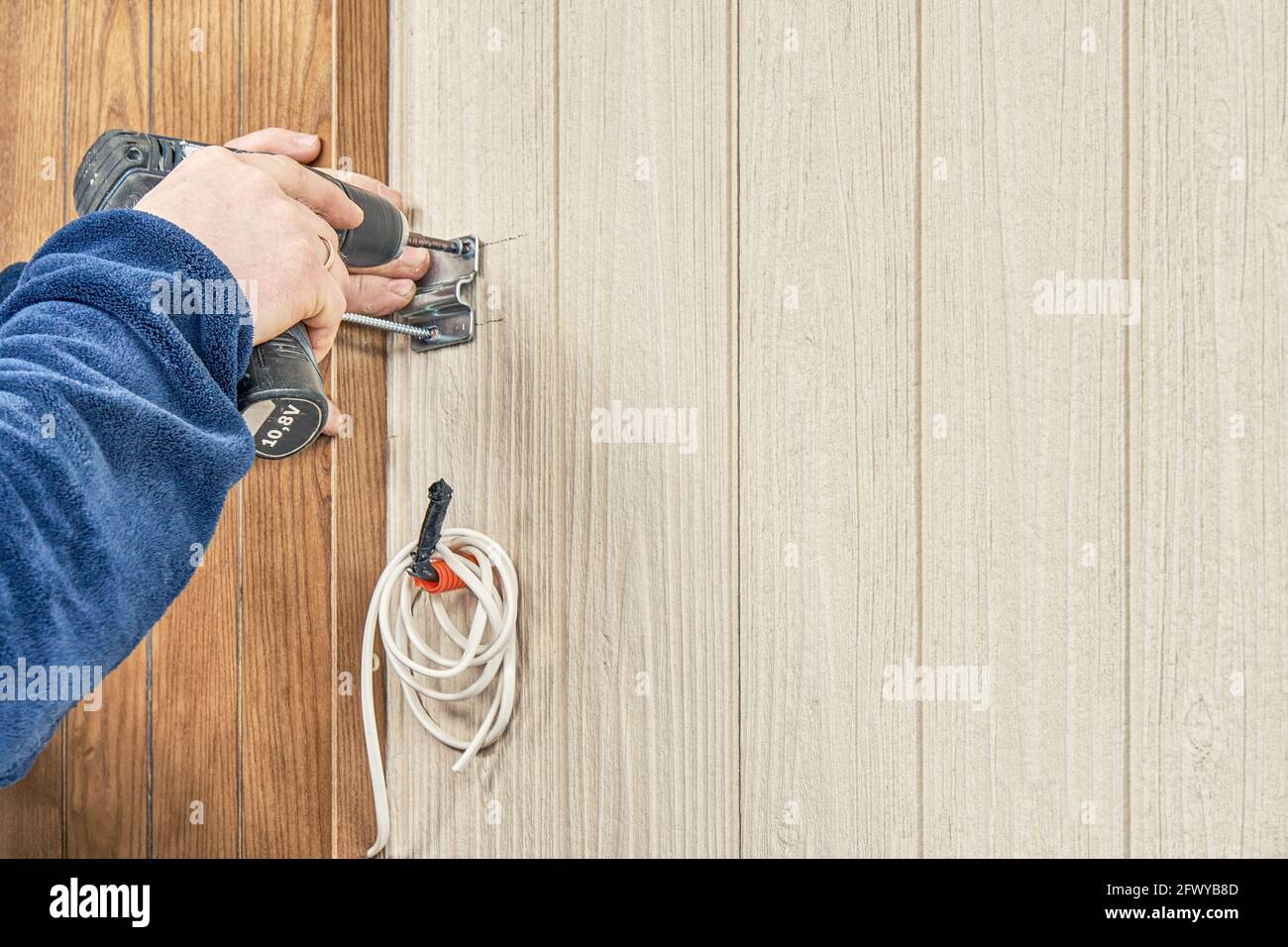 Craftsman in blue jacket fastens metal attachment plate for lamp on wooden wall with electrical screwdriver outdoors closeup Stock Photo