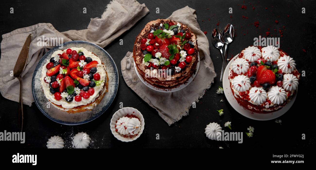Assorted delicious and colorful homemade cakes with different type of filling on black background. Panorama Stock Photo
