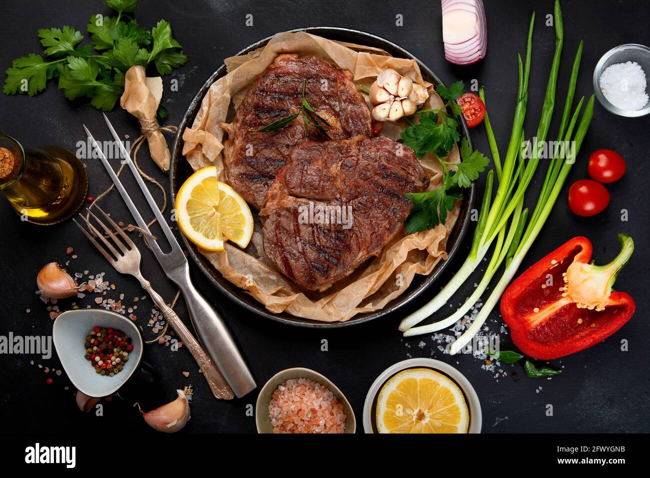 Delicious prepared meat steaks with seasoning and herbs on dark background. Geilled food concept. Top view Stock Photo
