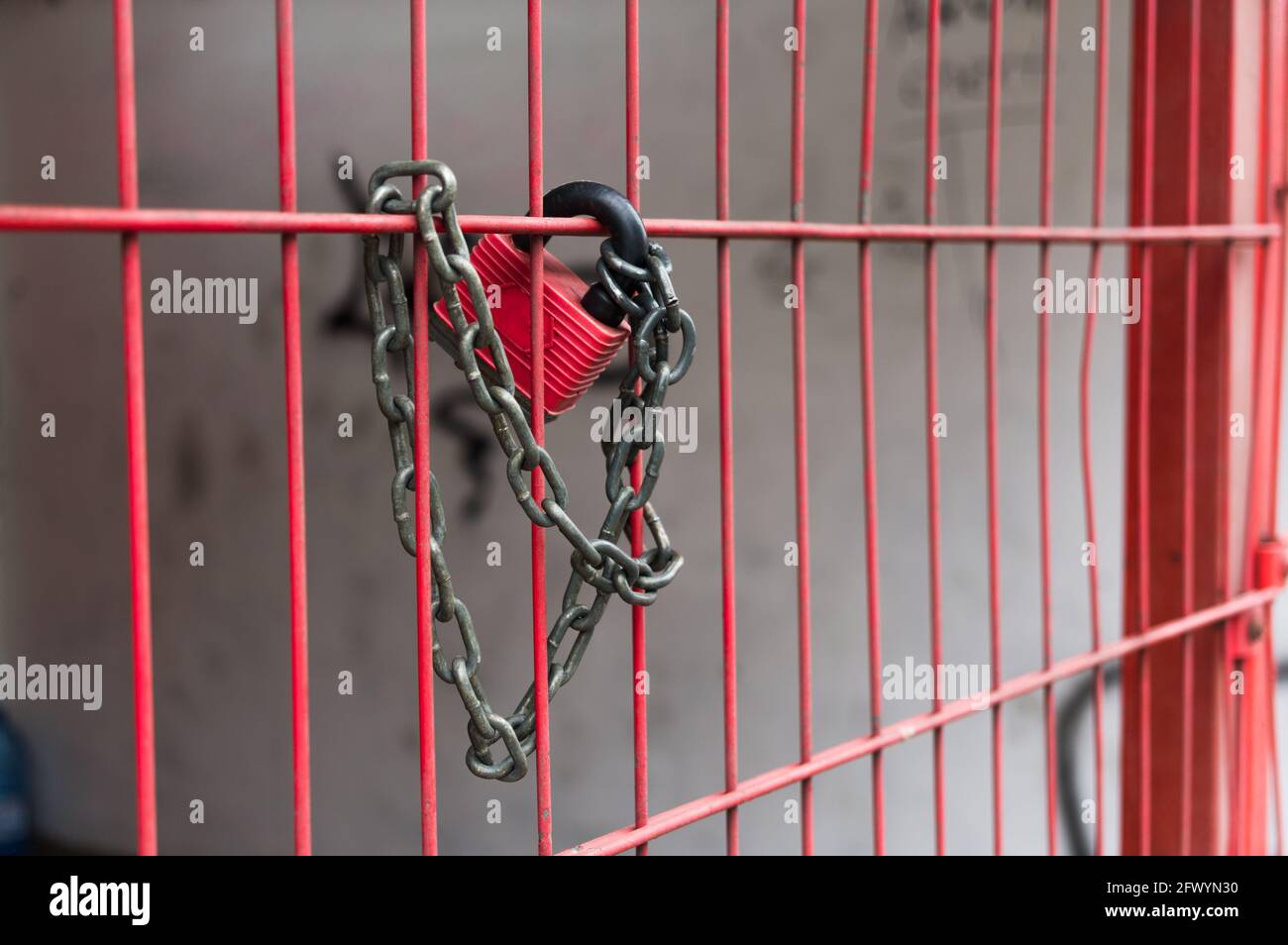 Red padlock with a chain on a red fence. The gate is locked with a