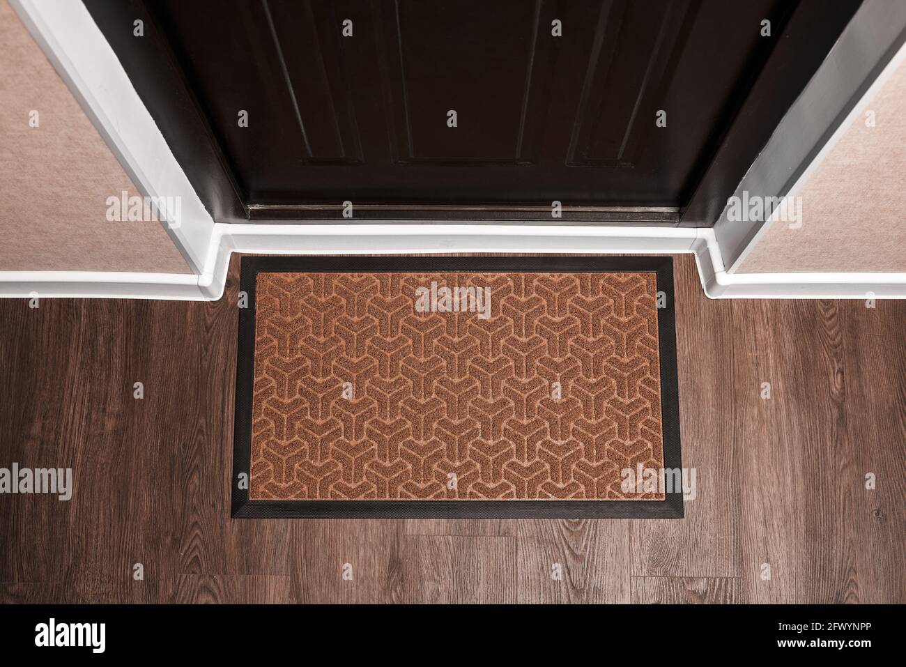 Blank doormat before the dark door in the hall. Top view of mat on wooden floor. Mockup for your design Stock Photo