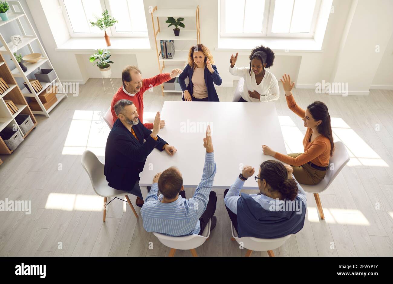 Group of people raising hands and voting in corporate meeting around office table Stock Photo