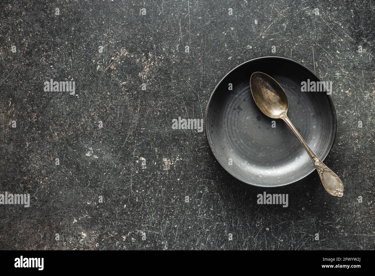 Empty vintage plate with silver spoon on black table. Top view. Stock Photo