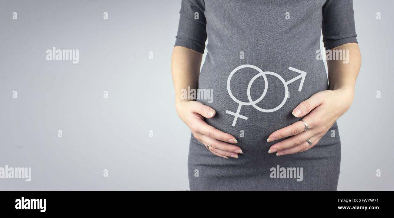Pregnant woman touching her belly with hologram male and female gender symbol, preparation and expectation concept. Close-up, copy space. Stock Photo