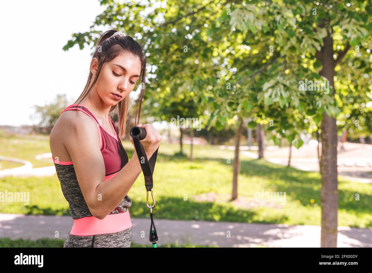 young caucasian woman exercising he biceps on a park. She is using resistance bands Stock Photo