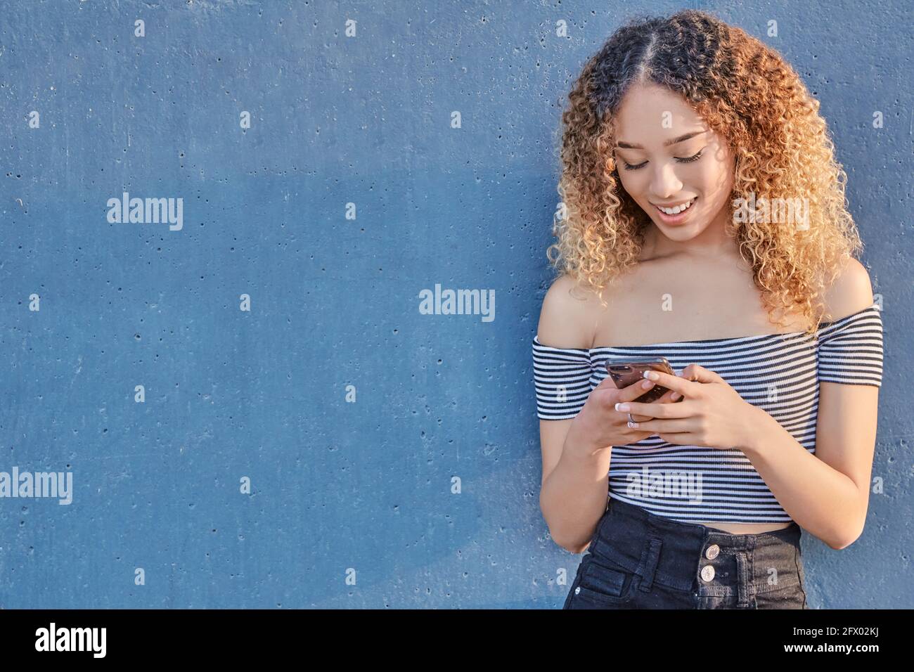 Smiling teenage latina girl holding smart phone using mobile app technology at home. Happy young Hispanic girl texting, checking social media apps. High quality photo Stock Photo