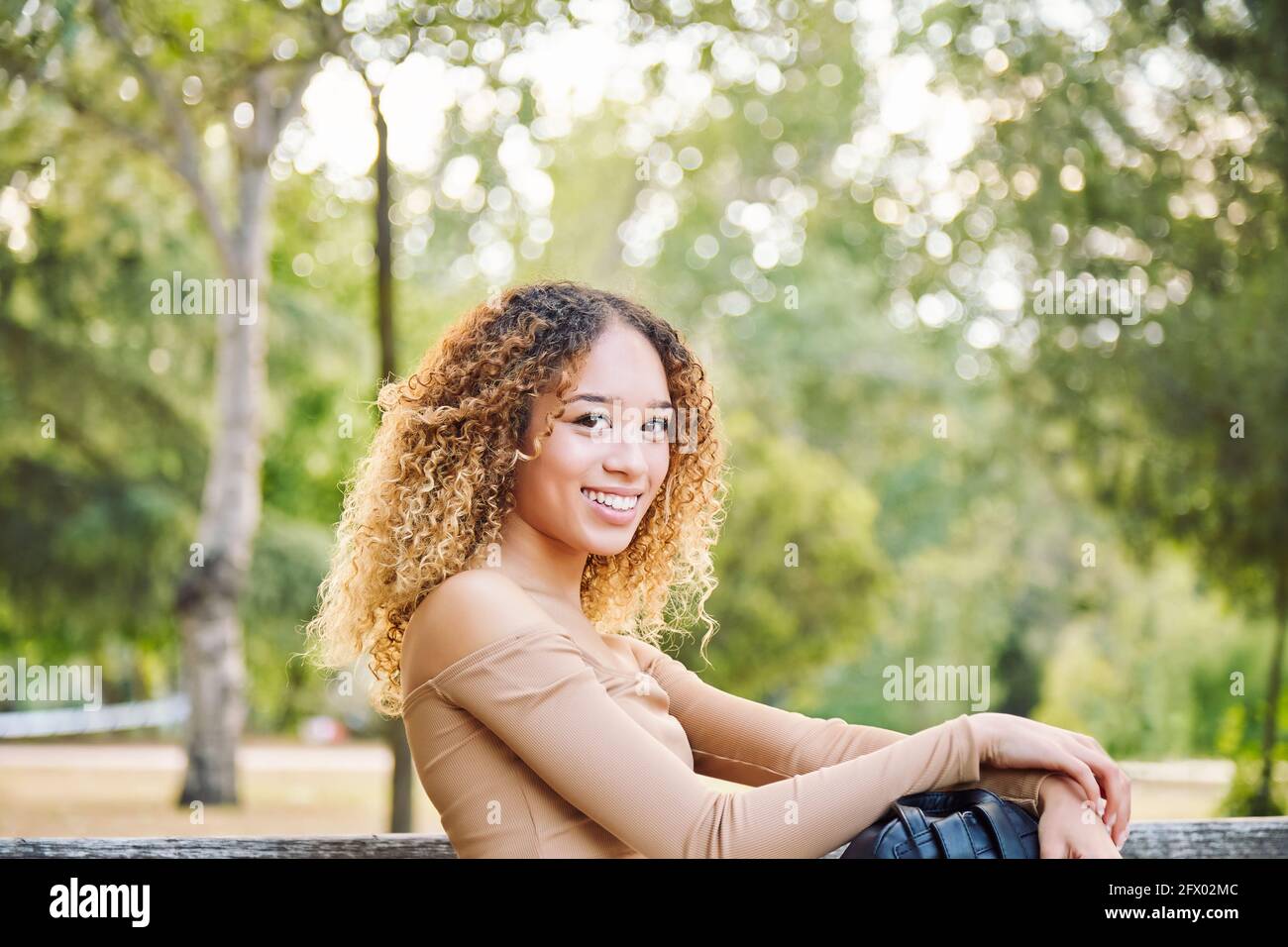 Woman with afro hair, in the forest having fun happy. Latina girl sitting on park bench. High quality photo Stock Photo