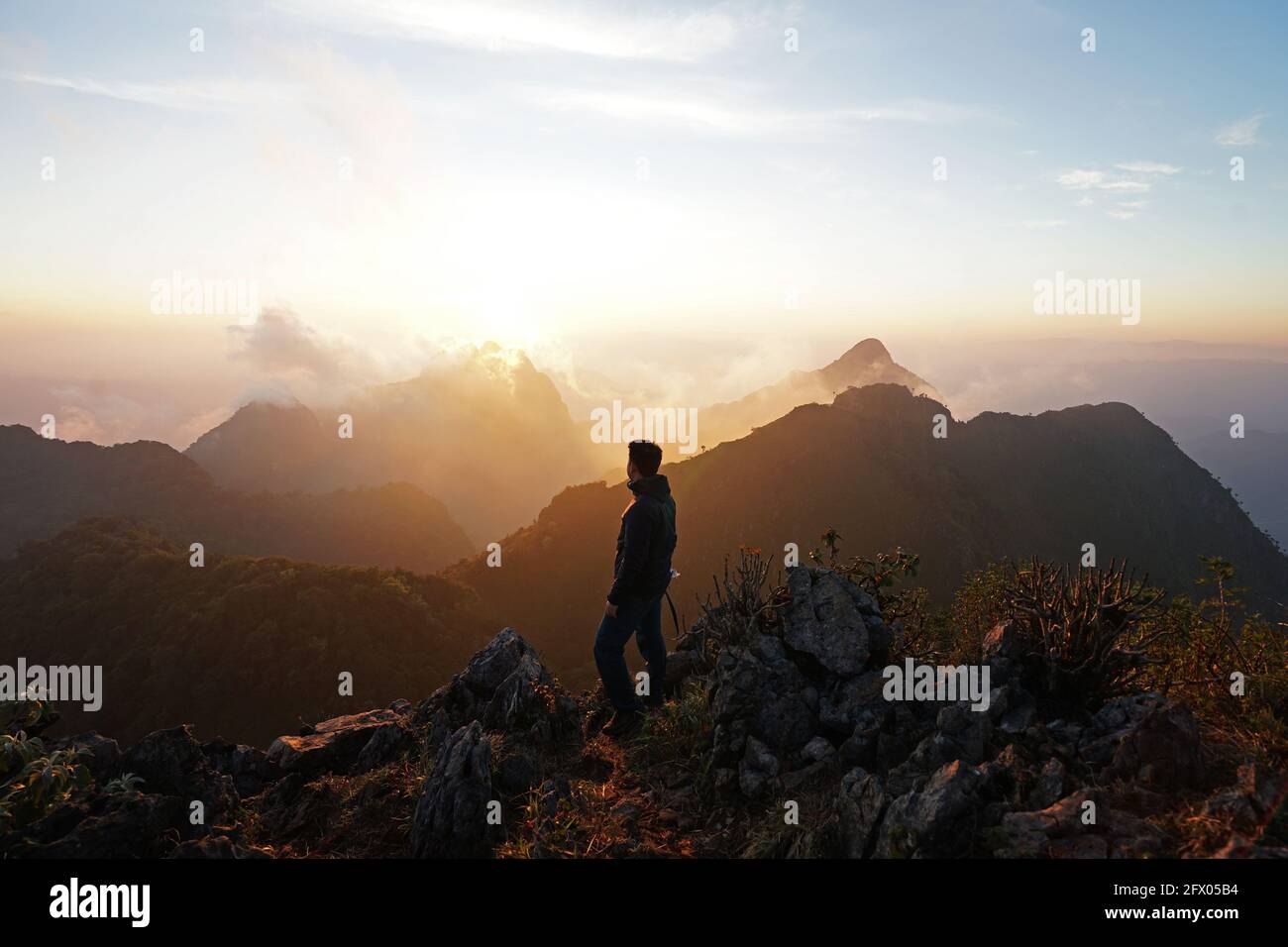 A man standing on the peak looking at green mountain range with cloudy ...
