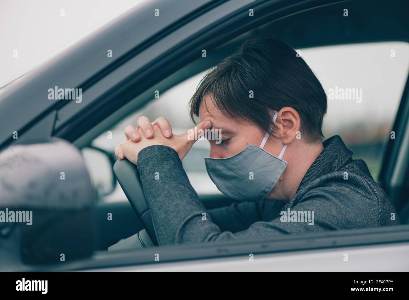 Disappointed female driver with protective face mask sitting in the car during Covid-19 pandemics, leaning her head on to steering wheel, selective fo Stock Photo