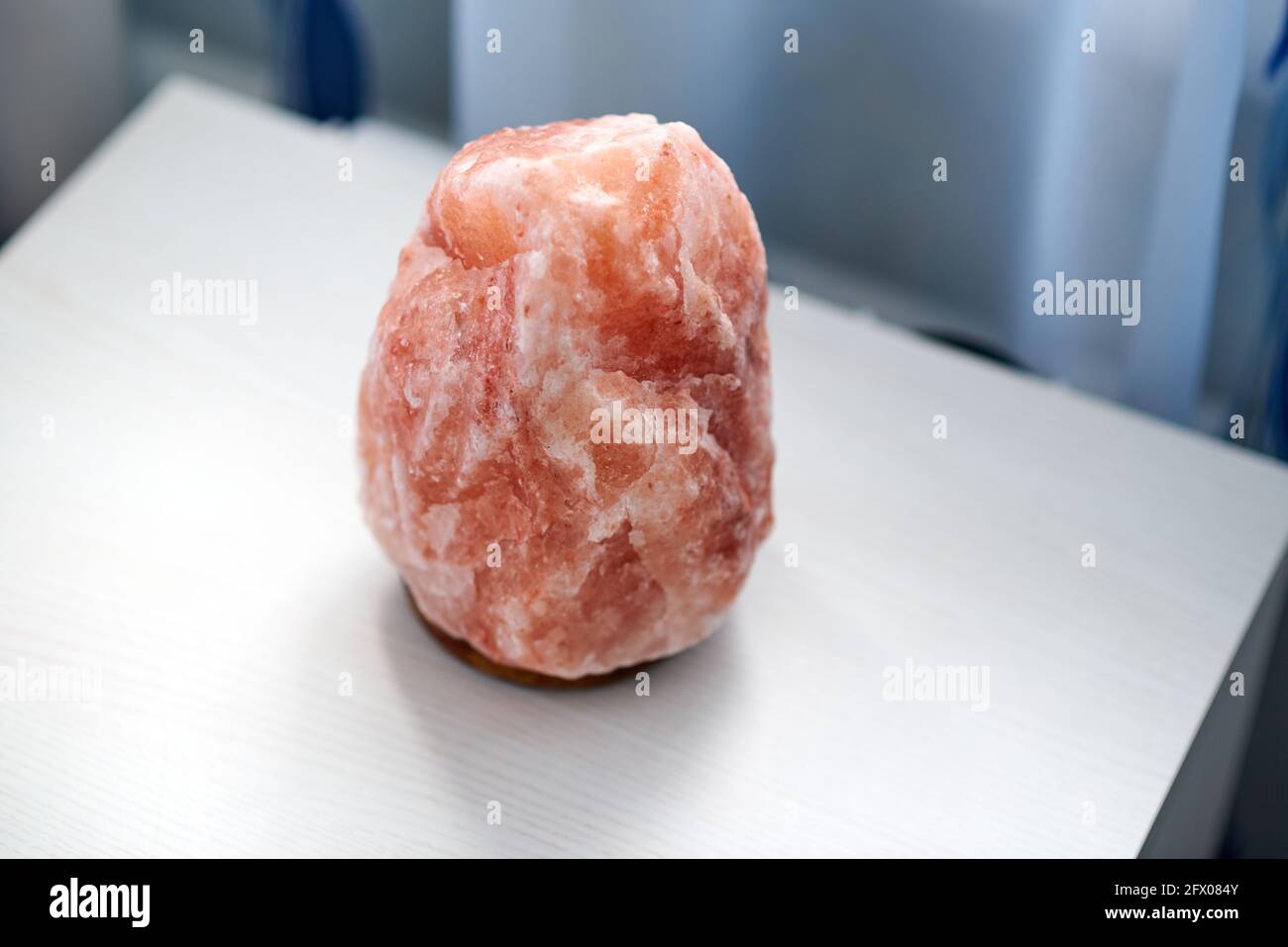 An orange salt lamp stands on a white bedside table Stock Photo