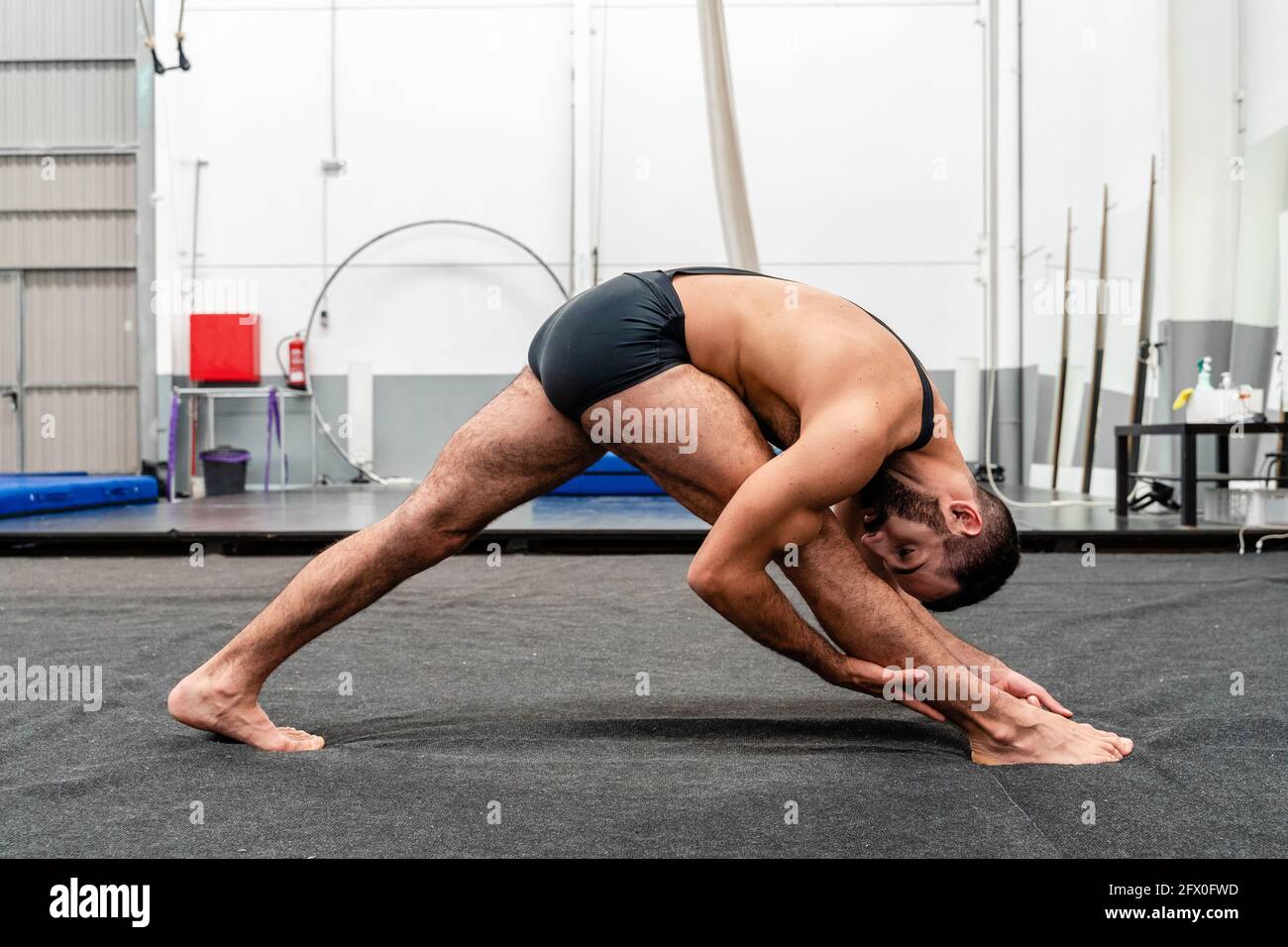 Full body fit flexible male in sports shorts doing Triangle Pose and looking at camera while practicing yoga in modern fitness center Stock Photo