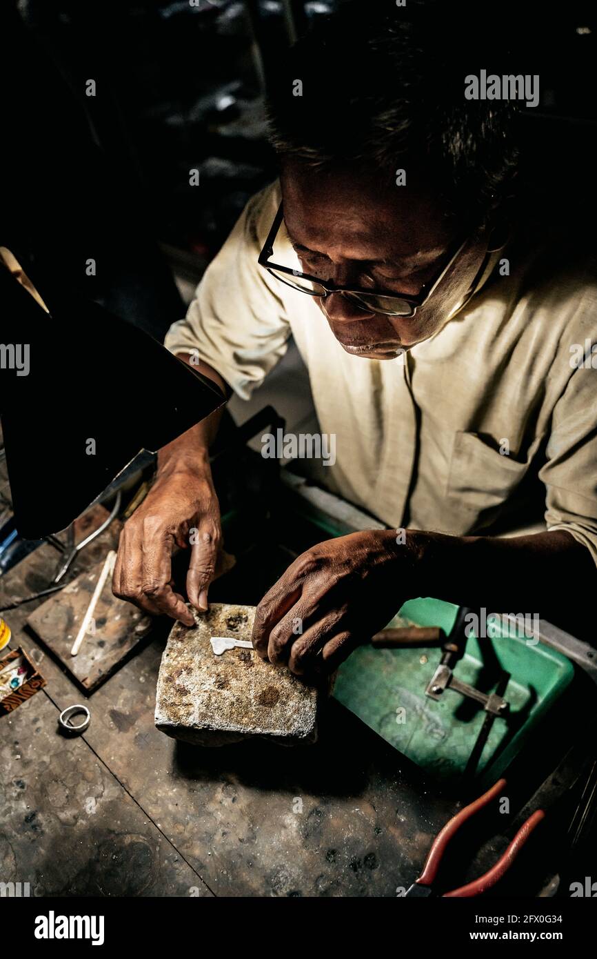 From above mature ethnic man working at weathered desk in craft workshop Stock Photo