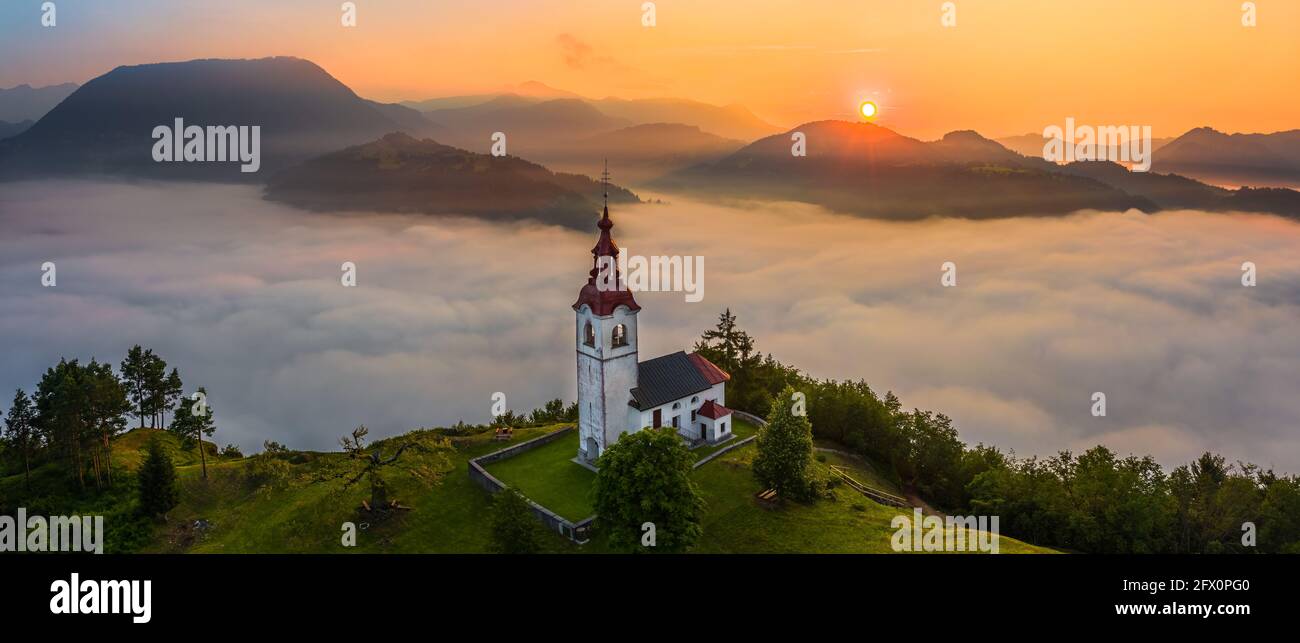 Sebrelje, Slovenia - Aerial panoramic drone view of the beautiful hilltop church of St.Ivan (Sv. Ivan Cerkev) at sunrise with huge morning fog bellow Stock Photo