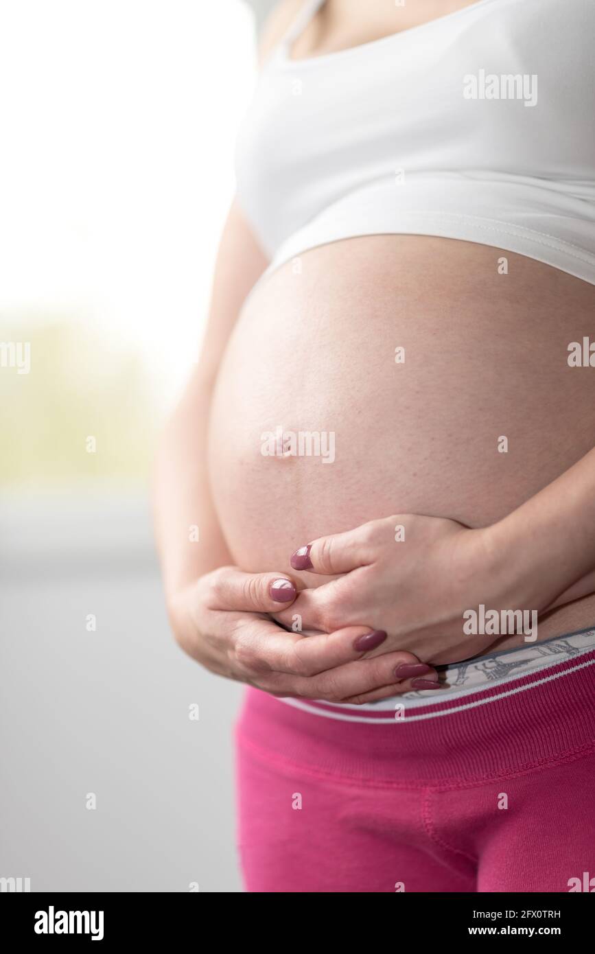 Pregnant woman holding hands on her belly Stock Photo - Alamy