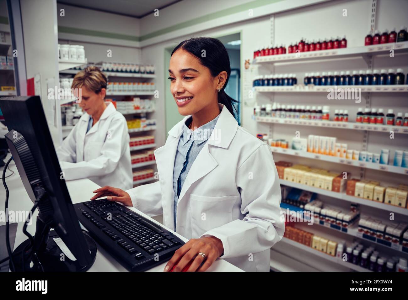 Young female pharmacist using computer with senior colleague using digital tablet in chemist Stock Photo