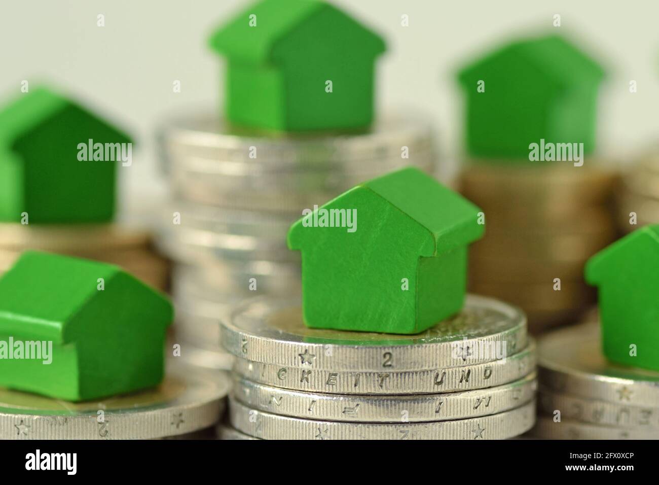 Close-up of green miniature houses on coin stacks - Concept of real estate investment, mortgage, home insurance and loan, eco-friendly house Stock Photo