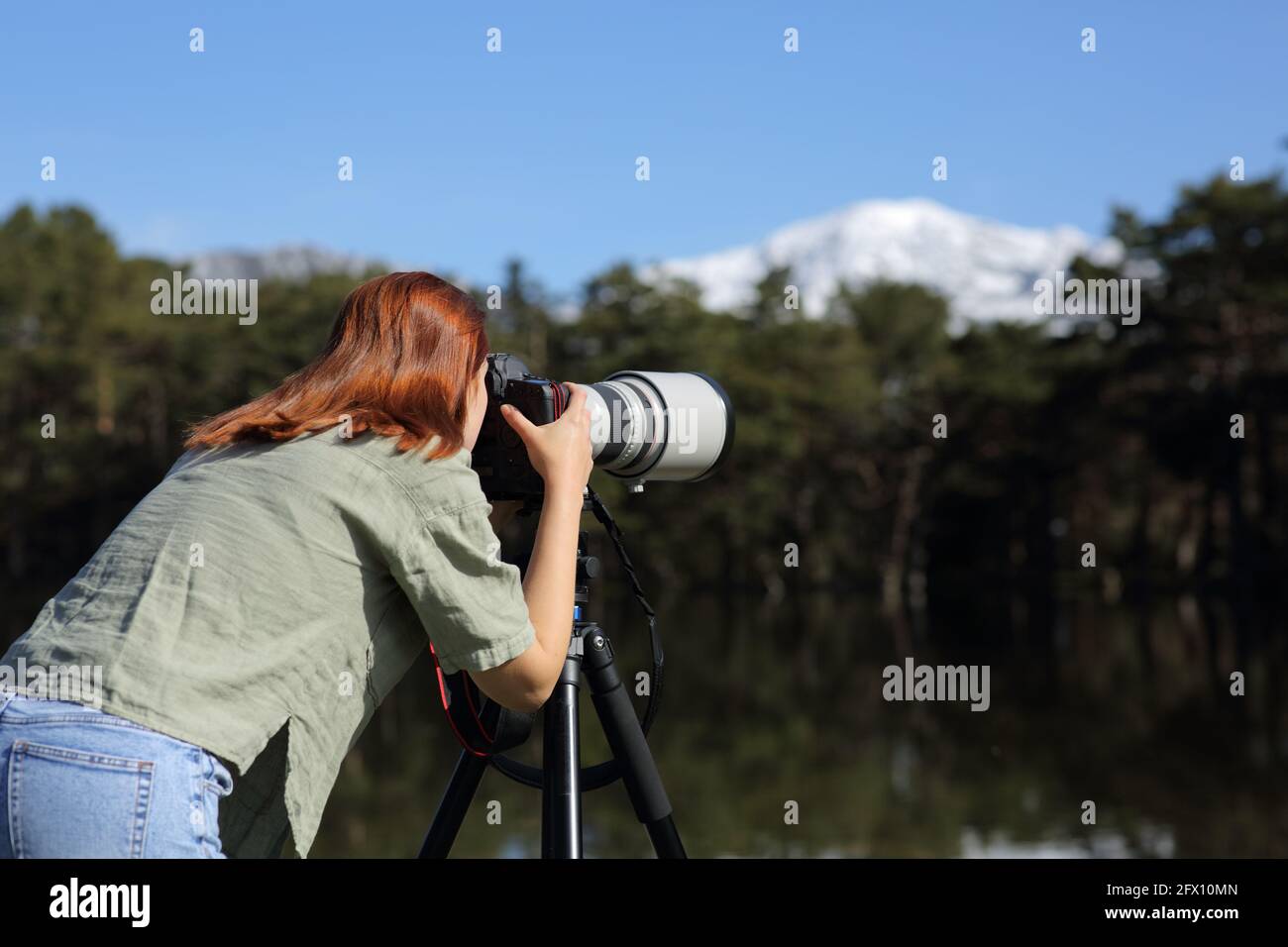Back view of a photographer taking pphotos with tele lens and dslr camera in the mountain Stock Photo