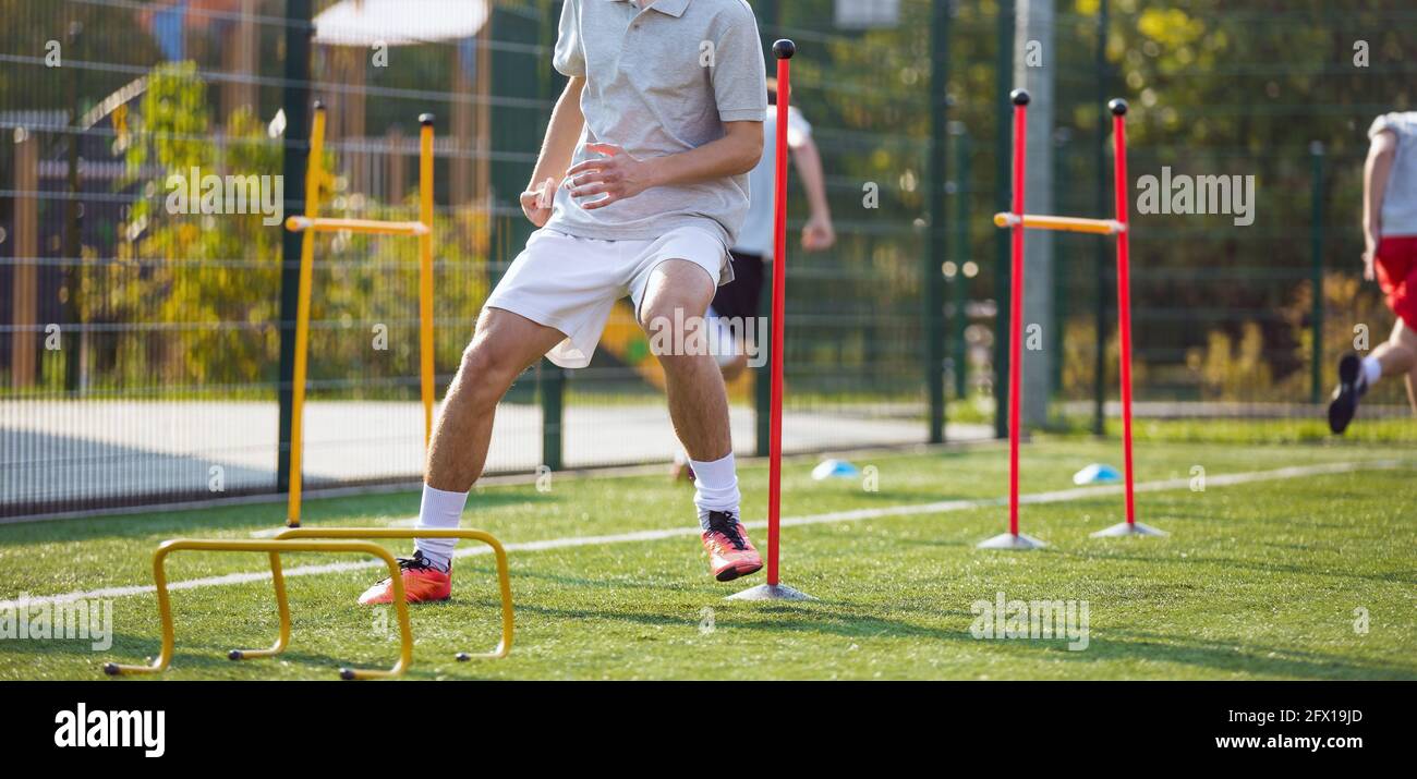 Teenage Football Players on Training Camp. Young Boys Running Slalom Track Between Training Poles and Jumping Over Hurdles. Soccer Training Equipment Stock Photo